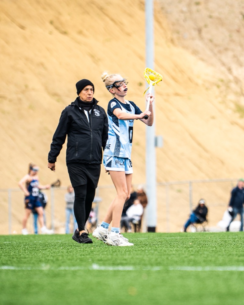 An FLG coach walking the field beside a player during a game.