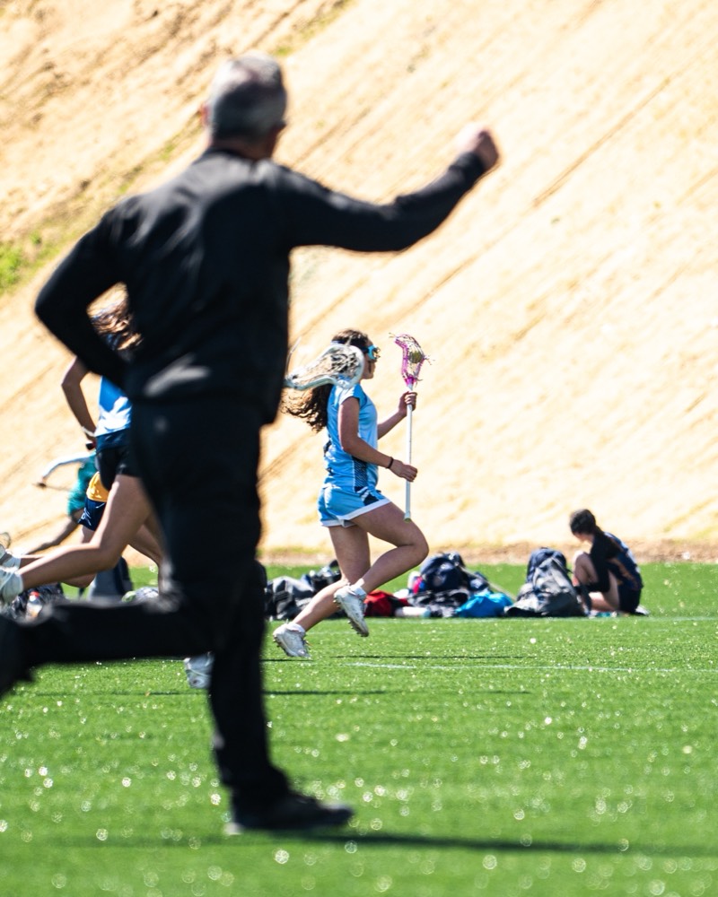 An FLG coach moving down the sideline as play runs past.