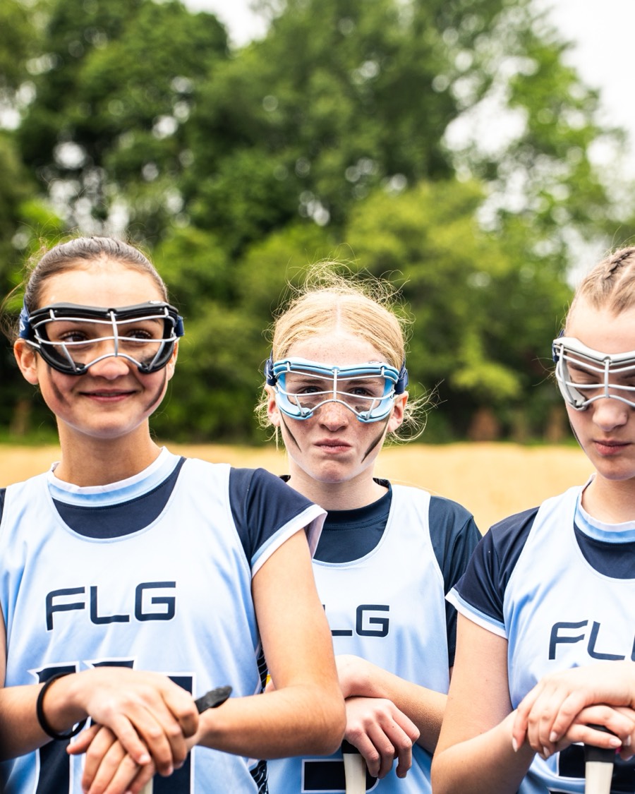 Three FLG players in goggles leaning on their sticks, watching from the sideline.