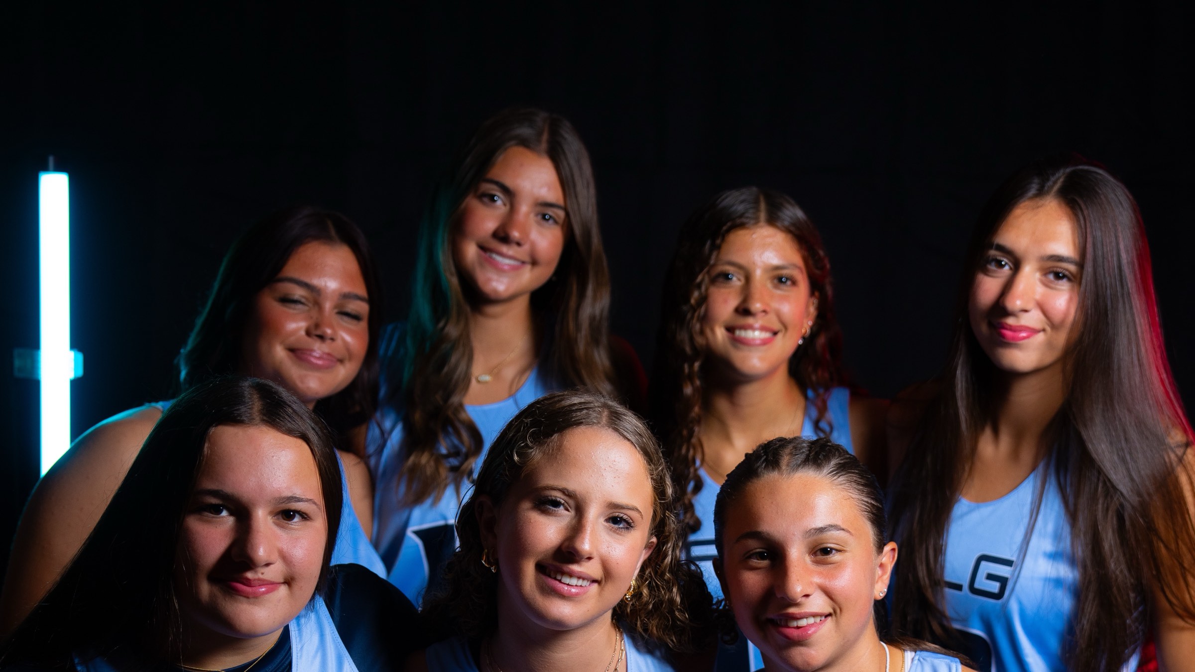 Seven FLG high school players in Carolina blue uniforms, smiling together at Media Day.